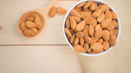 Almonds raw peeled in white porcelain bowl with wooden spoon on wooden table background.Healthy food Concept.