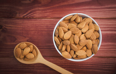 Almonds raw peeled in white porcelain bowl with wooden spoon on wooden table background.Healthy food Concept.