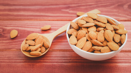 Almonds in wood spoon with white porcelain bowl on wooden table background.Healthy food Concept.