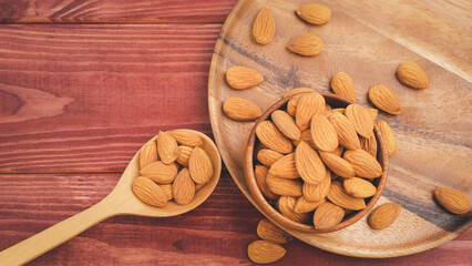 Almonds pour from wood spoon with brown wooden bowl on wooden table background.Healthy food Concept.