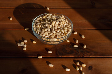 Pine nuts in bowl under natural sunlight on wooden table. Healthy food and snack