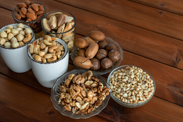 Mixed nuts in bowl on wooden table. Walnut, pecan, almonds, hazelnuts, macadamia, cashews and pine nuts