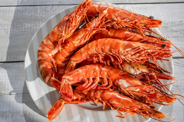 Close-up giant deep-sea shrimps gambas. Boiled prawns on white plate, top view, on wooden background.