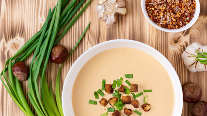 Delicious chestnut soup on a wooden background with seasonings and onions. Top view.