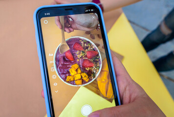 Selective focus A woman photographs a Healthy food Acai breakfast superfoods smoothie bowl with...