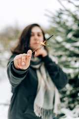 Adult young woman with sparklers on the background of winter pine forest