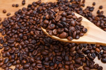 A group of coffee beans in the wooden spoon on top of a pile of coffee beans 