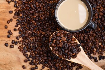 Top view of coffee beans in the wooden spoon with a cup of coffee and a pile of coffee beans 