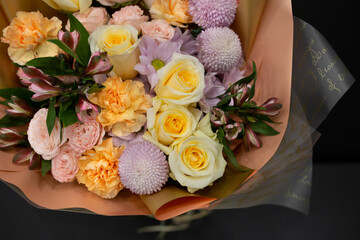 A bouquet of flowers with yellow roses and other flowers in decorative packaging on a dark background.