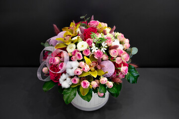 Floral arrangement with orchids, cotton and other flowers in a large hat box on a dark background.