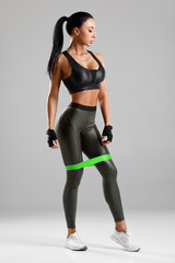 Fitness woman with resistance band on the gray background. Sporty girl training