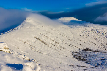 Hikers and walkers on a cold, snow covered mountain in the early morning sunshine (Pen-y-Fan)