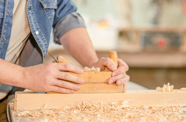 Close up mans hands planing wood in a workshop