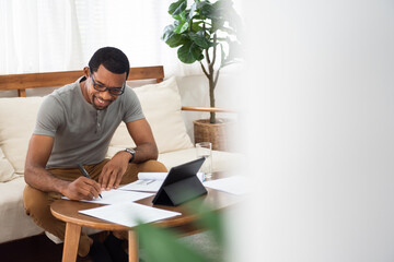 Happy Smiling African American man working on paperwork and digital tablet at home office.