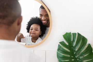 African American Father and Son looking at mirror brushing teeth in bathroom.