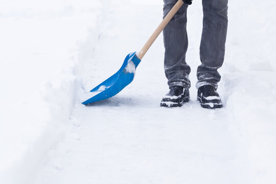 Man shoveling fresh white snow with blue shovel on sidewalk after blizzard in winter day. Closeup.