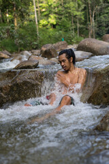 Fototapeta na wymiar A male traveler enjoying the cold of rainforest stream during morning.Man shower in the waterfall pool.
