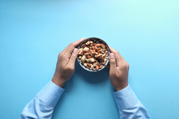 top view of hand holding a bowl of mixed nut on blue background 