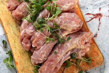 Raw Chicken neck decorated with green sprouts on a kitchen wooden board on a light marble background