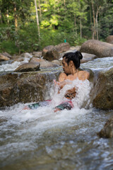 A male traveler enjoying the cold of rainforest stream during morning.Man shower in the waterfall pool.