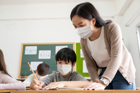 Young Asian Teacher with little boy wearing protective face masks studying in classroom