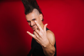 Punk with black electric guitar, mustache and big mohawk showing horn gesture. Photo of a rock...