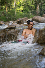 A male traveler enjoying the cold of rainforest stream during morning.Man shower in the waterfall pool.