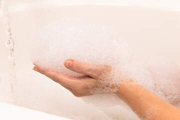 soap foam forms on a woman's hand in the bathroom, a stream of water. background light tile