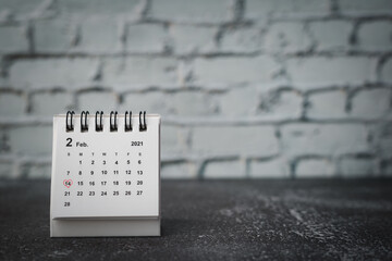 Calendar with red heart shaped marking on date February, 14 against blurred brick background for...