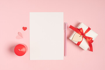 Desktop blank paper note pad. Flat lay of pink pastel working table background with Valentine gift, letter, heart shape and decoration. Top view, mock up greeting card