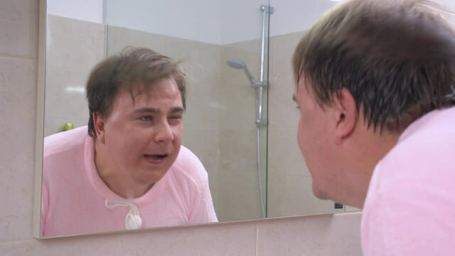 Young man in pink pajamas washes his face in bathroom in morning after waking up or in evening before going to bed. Strange loud sound caught attention of guy.