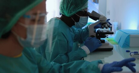 Medical workers in hazmat suit working with laptop computer and micoroscope inside lab hospital during coronavirus outbreak - Powered by Adobe