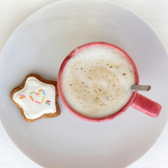 red mug with frothy cappuccino and cookies in the shape of a star decorated with a heart, top view. warming coffee with sweet dessert