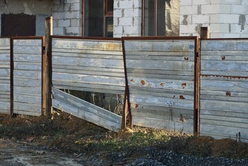 old gray gate with broken iron and brown rust and part of a fence on a rural street