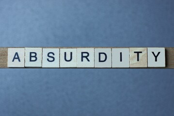 text the word absurdity from brown wooden small letters with black font on an gray table