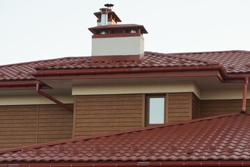 brown wooden attic of a private house with a window and part of a red tiled roof with a chimney against a gray sky