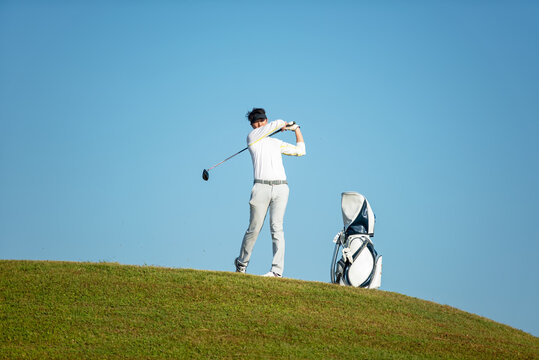 Golfer asia man approach on tee off for swing and hitting golf ball on slope green and looking fairway in course. Hobby playing game golf in holiday and vacations day on club golf.
