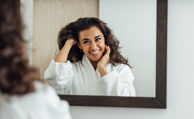 Beautiful middle east woman with long brown hair looking at a mirror in bathroom and smiling
