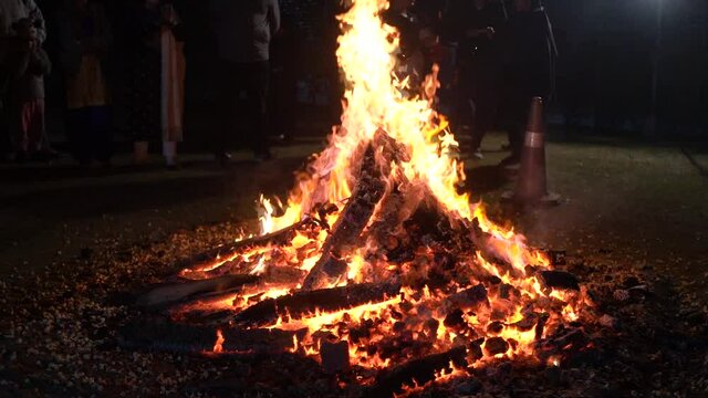 Men women families standing around giant blazing wood fire on lohri holi festival in india