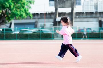 Agile children jogging in exercise stadium. Cute girl wearing white pants and sports shoes. Asian child jogging to keep their bodies healthy. Winter in Thailand. Sun is warm. Happy kid is 3-4 years.