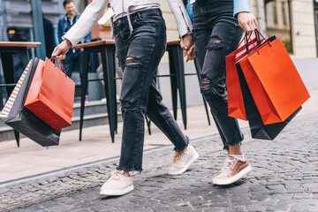 Close up photo of female legs stepping forward, in their hands shopping bags