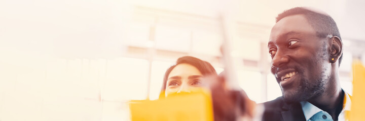 Background of business team brain storming using sticky note in foreground, pointing at note with a smile. Successful business Team concept. Banner frame.