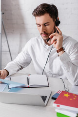 young interpreter in headset holding document near digital translator and dictionaries on blurred...