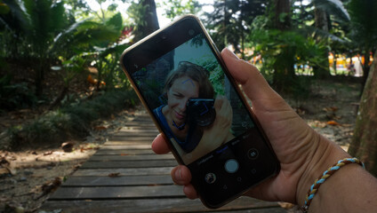 Selfie with smartphone of woman making photo on camera with tropical nature background