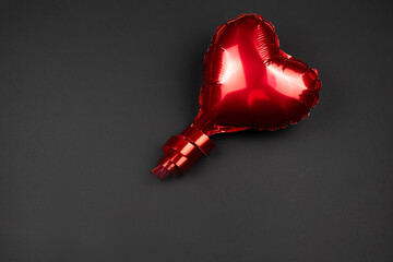 Red balloon in the shape of a heart on a black background.The concept of Valentine's day.