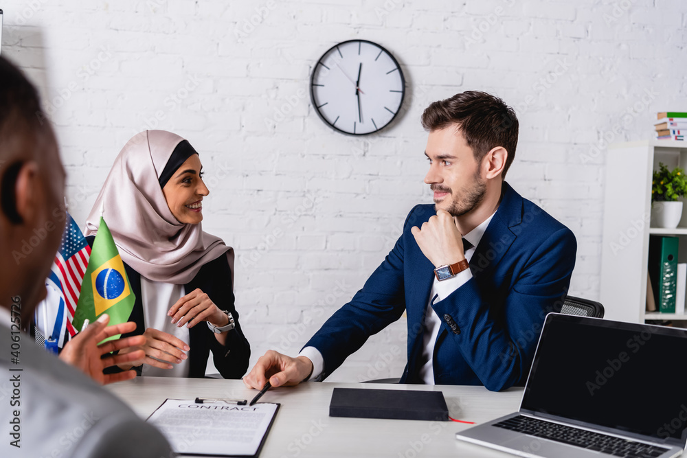 Sticker cheerful arabian businesswoman smiling during meeting with multicultural business partners, blurred 