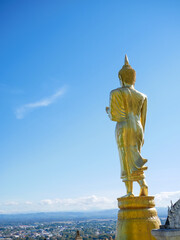 Rear view of ancient golden buddha statue on sky background located at famous landmark Wat Phra That Khao Noi in Nan province, Thailand. The temple is full of people believe , praying and meditating.