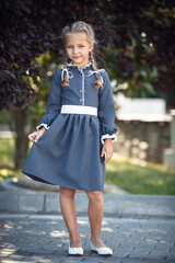 Charming little girl in a retro dress walking in the city on a sunny summer day. Little girl wear school uniform. Primary school girl with long hair. Study and education.