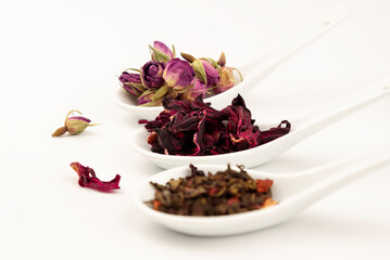 Three ceramic spoons with different tipe of teas: Hibiscus, Rose and Chai teas on white background.