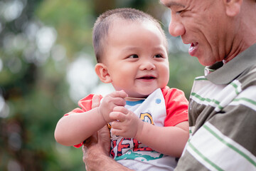 Portrait of adorable expressions of Asian little baby and grandfather on nature background with copy space,Cute boy, 7 months old, crawling age, good smile and good mood. Healthy, big black eyes.